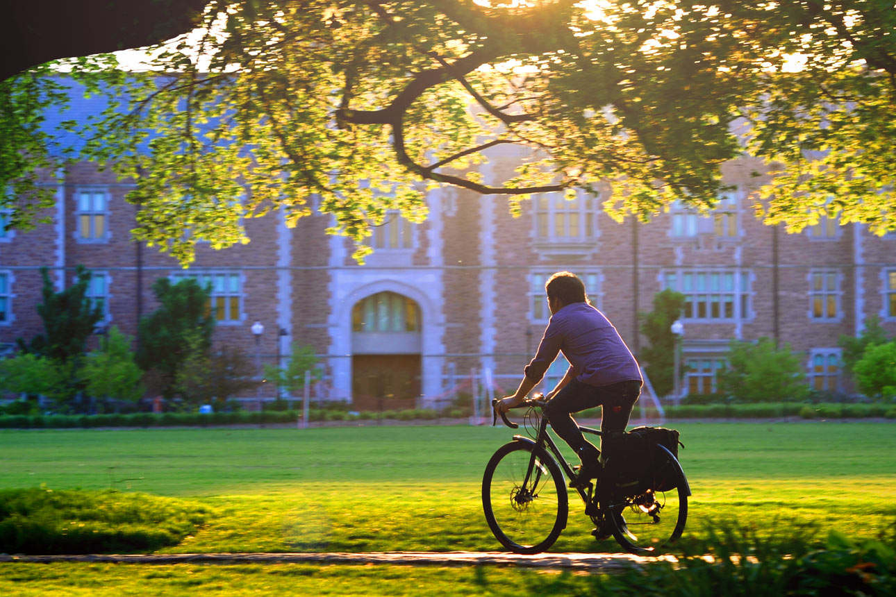 student riding bike on campus in-line